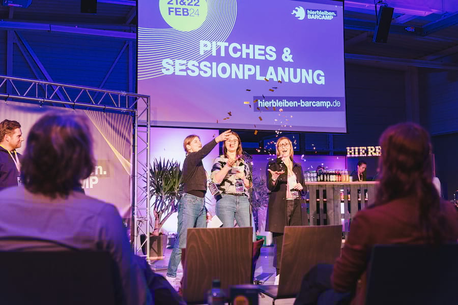 Pitchende Teilnehmende des BARCAMPS auf der Bühne